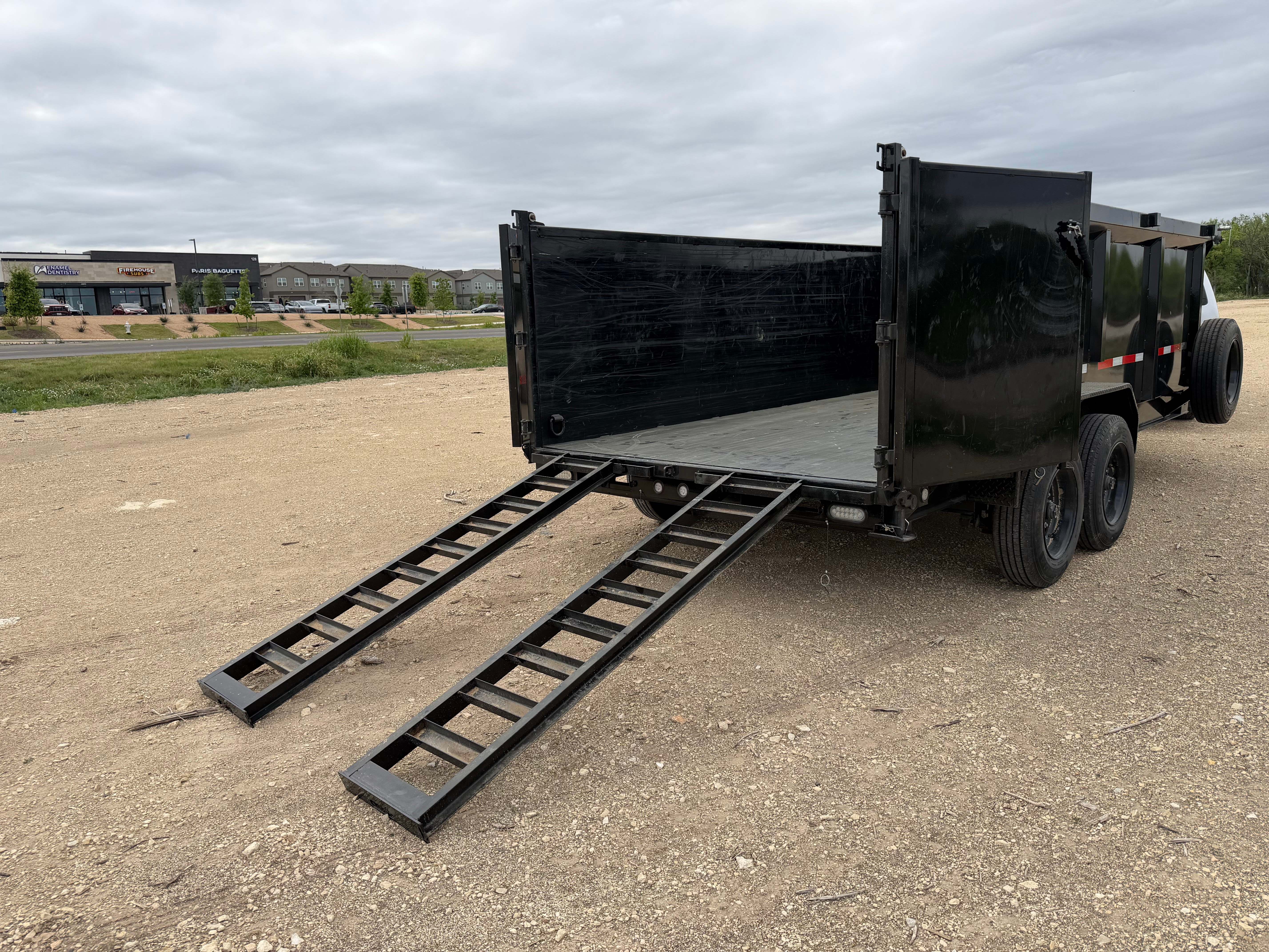 Maxx-D dump trailer rear view with ramp deployed on dirt road